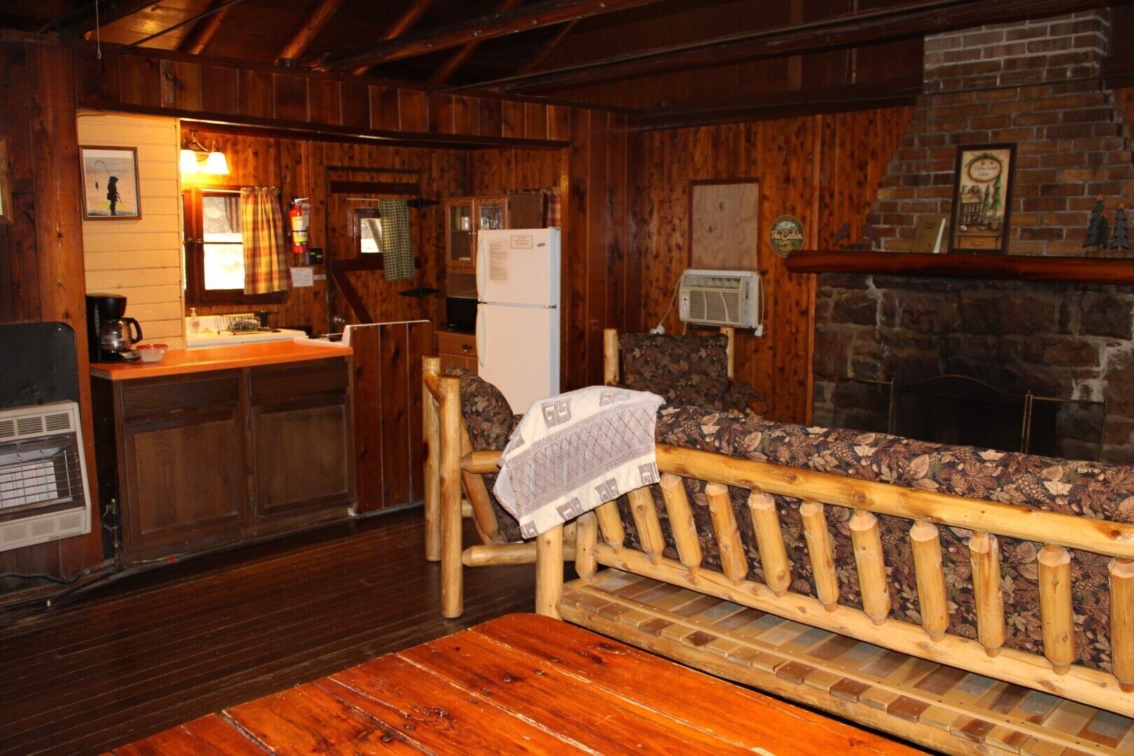 L’intérieur d’un chalet rustique, avec un banc en bois, un coin cuisine doté d’un réfrigérateur et une cheminée en pierre.