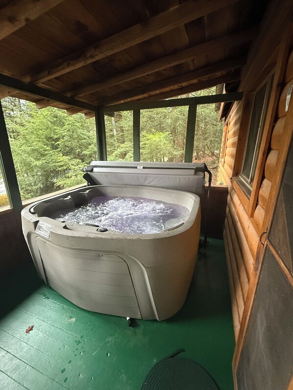 A hot tub in a wooden cabin with a view of trees through the windows.