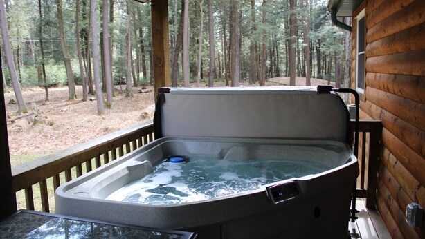 A hot tub in a wooden cabin with a view of a forest. - Hominy Ridge Cabins and Gift Shop (Clarington)