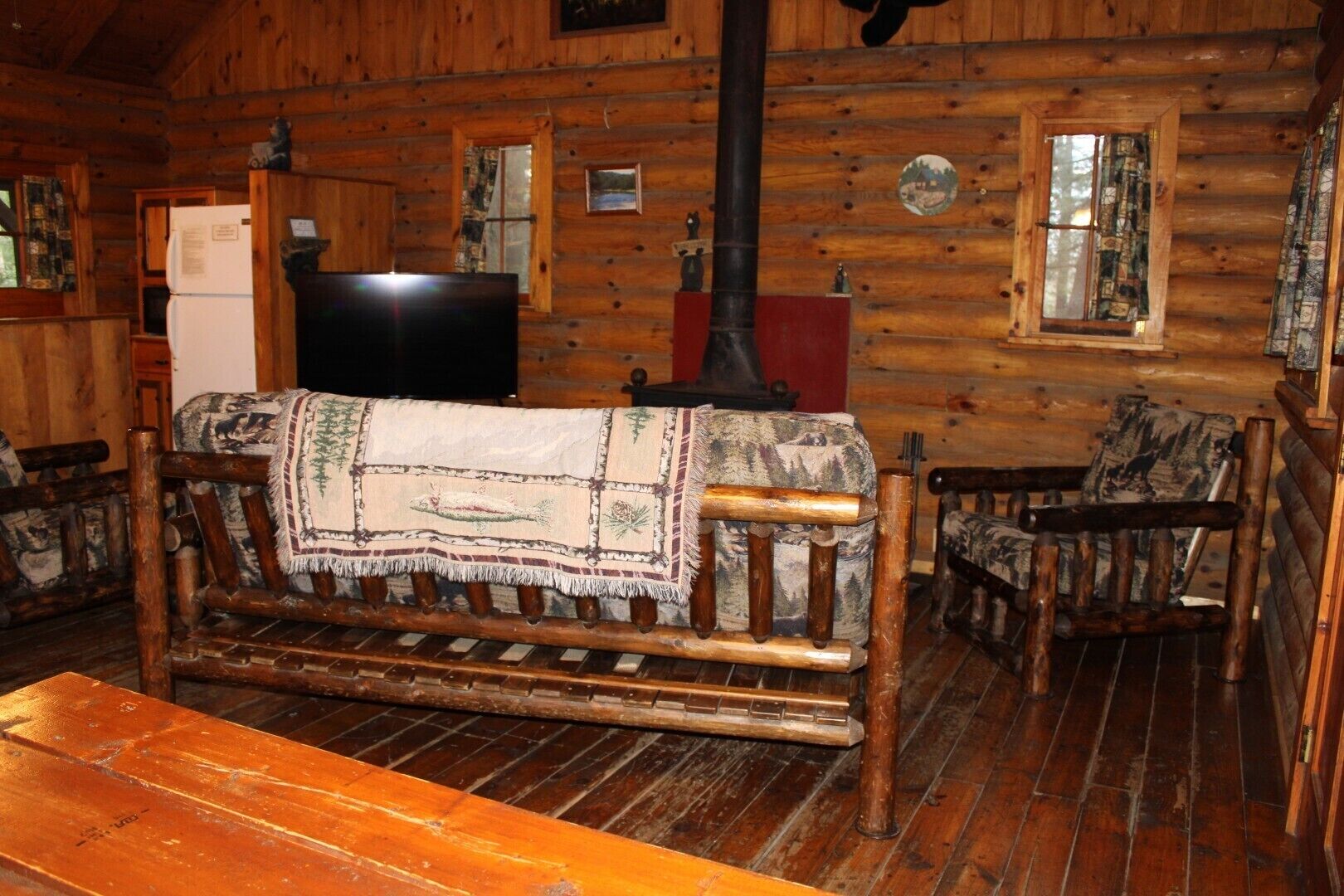 Interior rústico de una cabaña con un sofá de madera, un televisor y una chimenea.