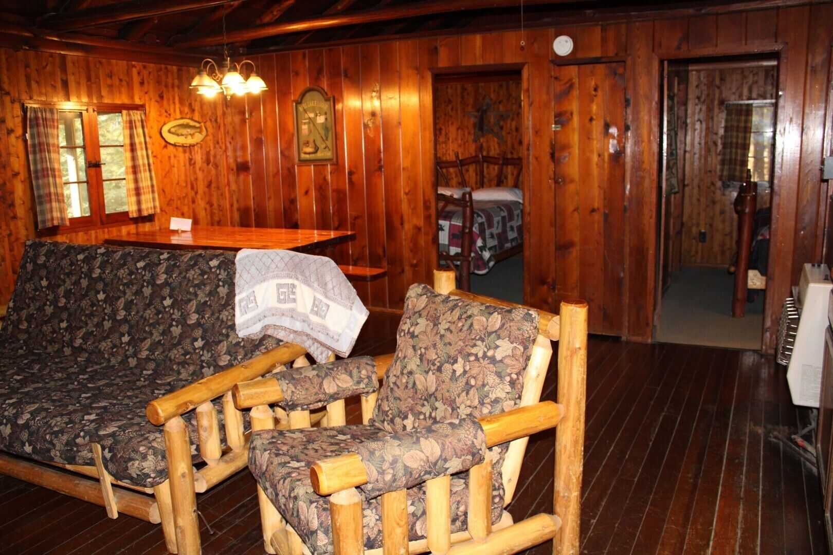 L’intérieur d’un chalet en bois, avec un canapé, deux chaises en bois, une table et un lit.