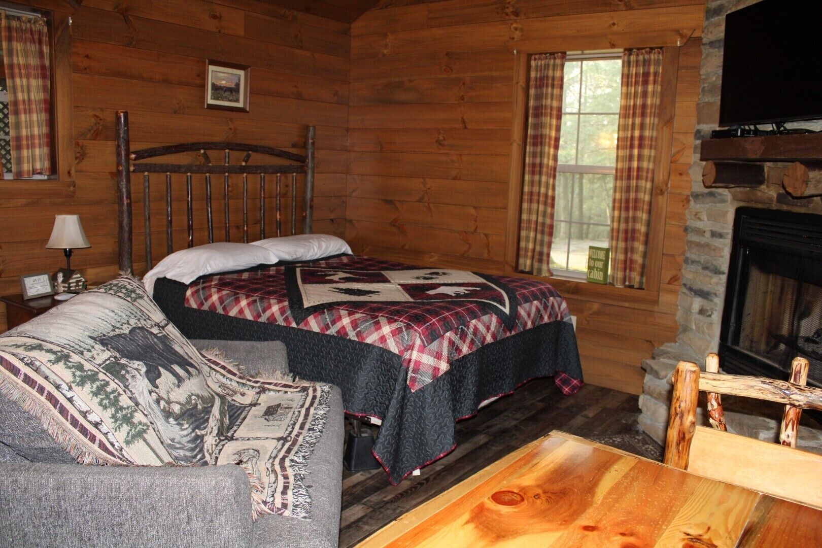 Una habitación de cabaña acogedora con una cama, un sofá, una chimenea y cortinas a cuadros.