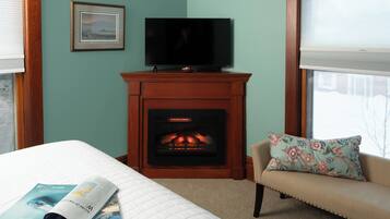 Una habitación con chimenea, un televisor en la pared, un sofá con un cojín floral y una cama con una revista encima.