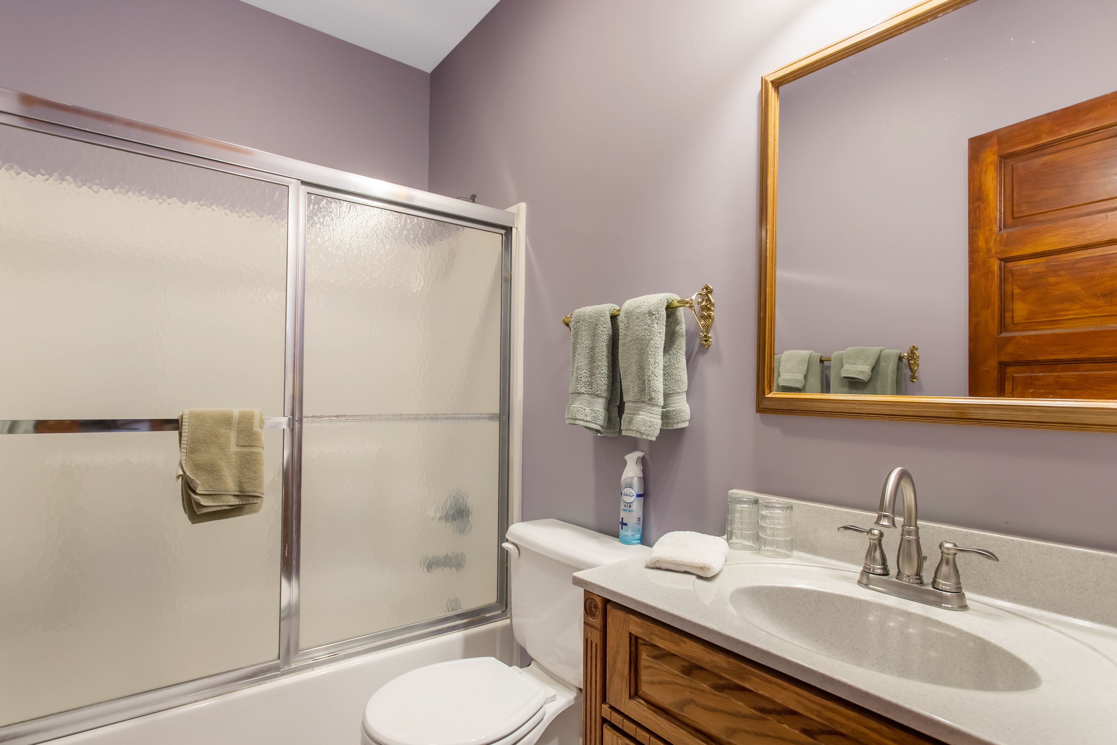 A bathroom with a glass shower enclosure, a white toilet, a wooden vanity with a sink, and a mirror above the sink.