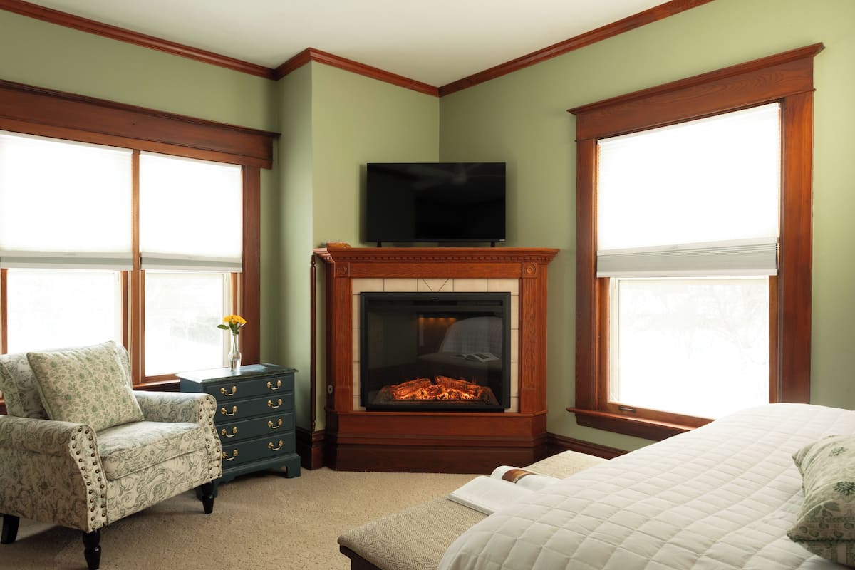 A room with a fireplace, a television, a bed, a chair, and a dresser.