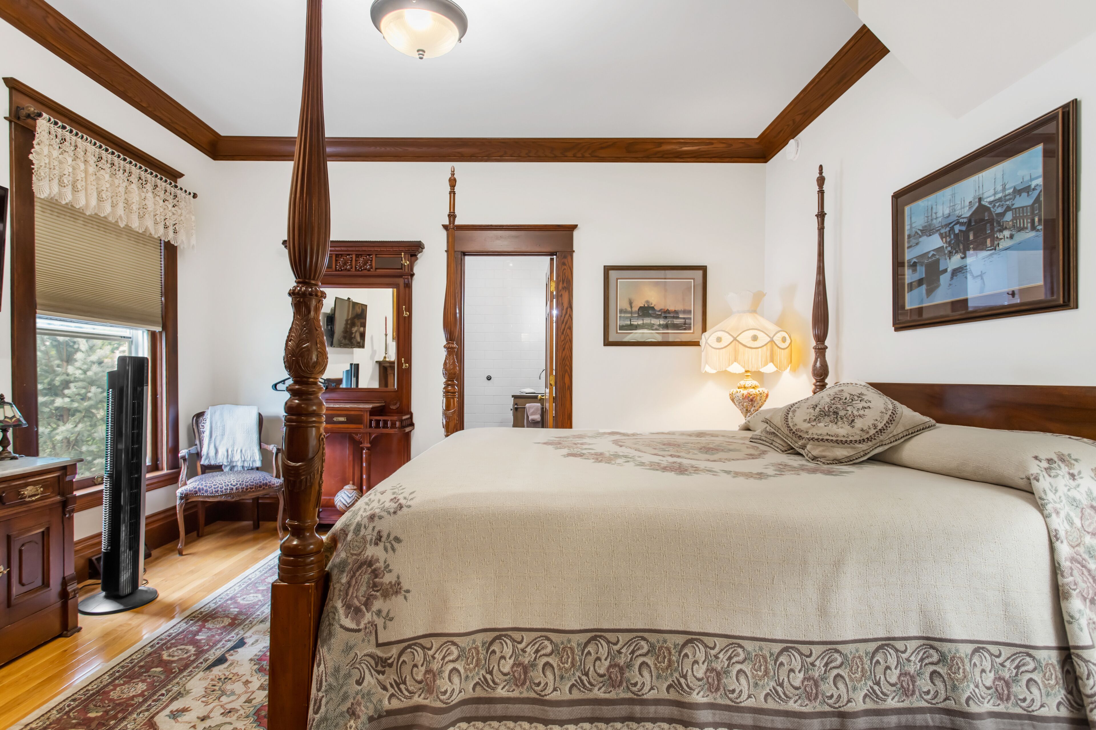 A traditional bedroom with a four-poster bed, wooden trim, a large mirror, and a framed picture on the wall.