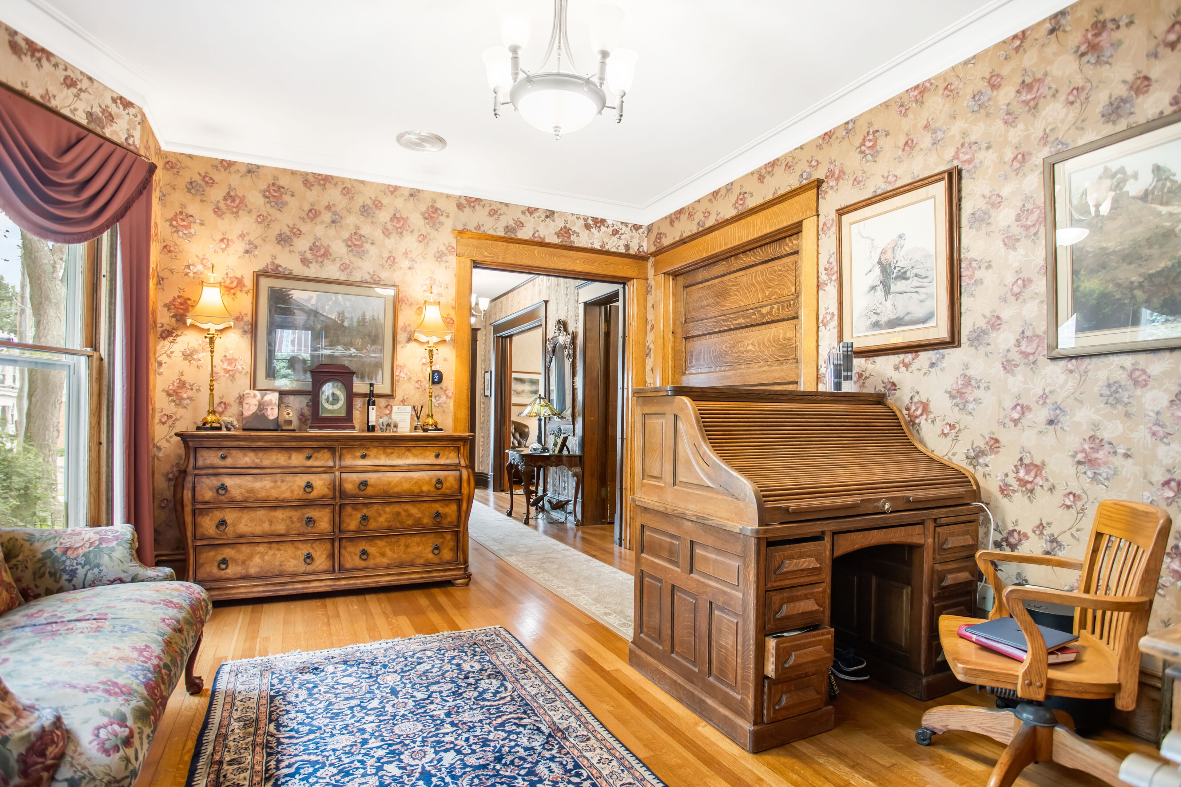 A room with a wooden desk, a chair, a dresser, and a bed with floral bedding.