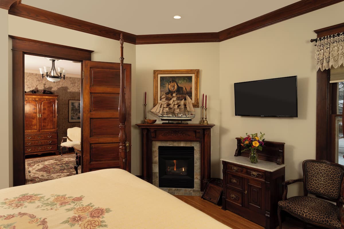 A bedroom with a fireplace, a television, a bed with floral bedding, a leopard print chair, and a wooden wardrobe.