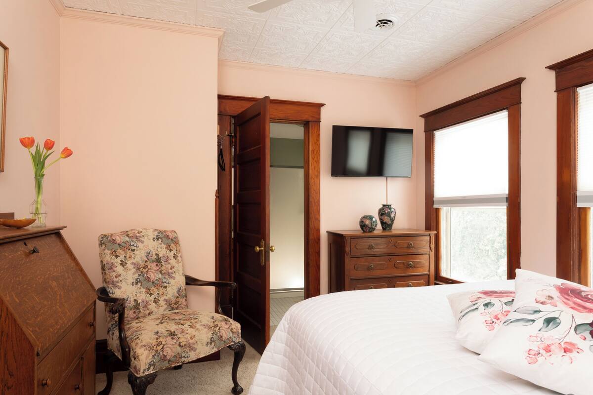 A bedroom with a bed, a chair, a dresser, a television, and a door leading to another room.