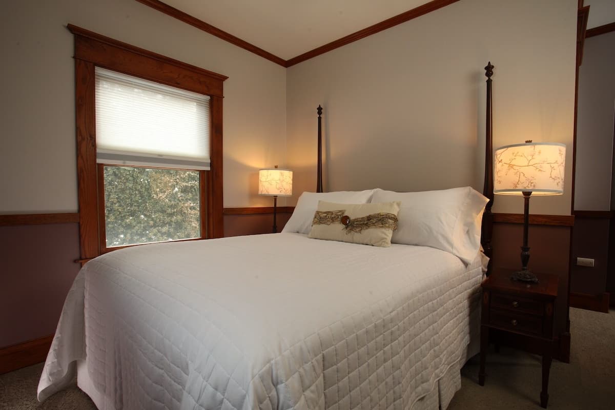 A neatly made bed with a quilted white bedspread, two pillows, and a nightstand with a lamp.