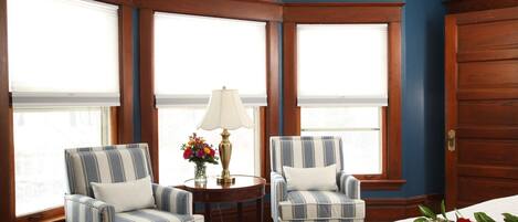 A room with two striped armchairs, a small table with a lamp, and a bed.