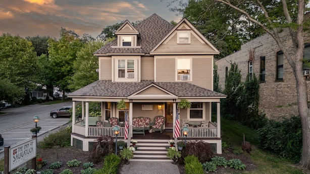 Una casa de dos pisos con un porche, banderas estadounidenses y un letrero que dice The Inn of Saugatuck.