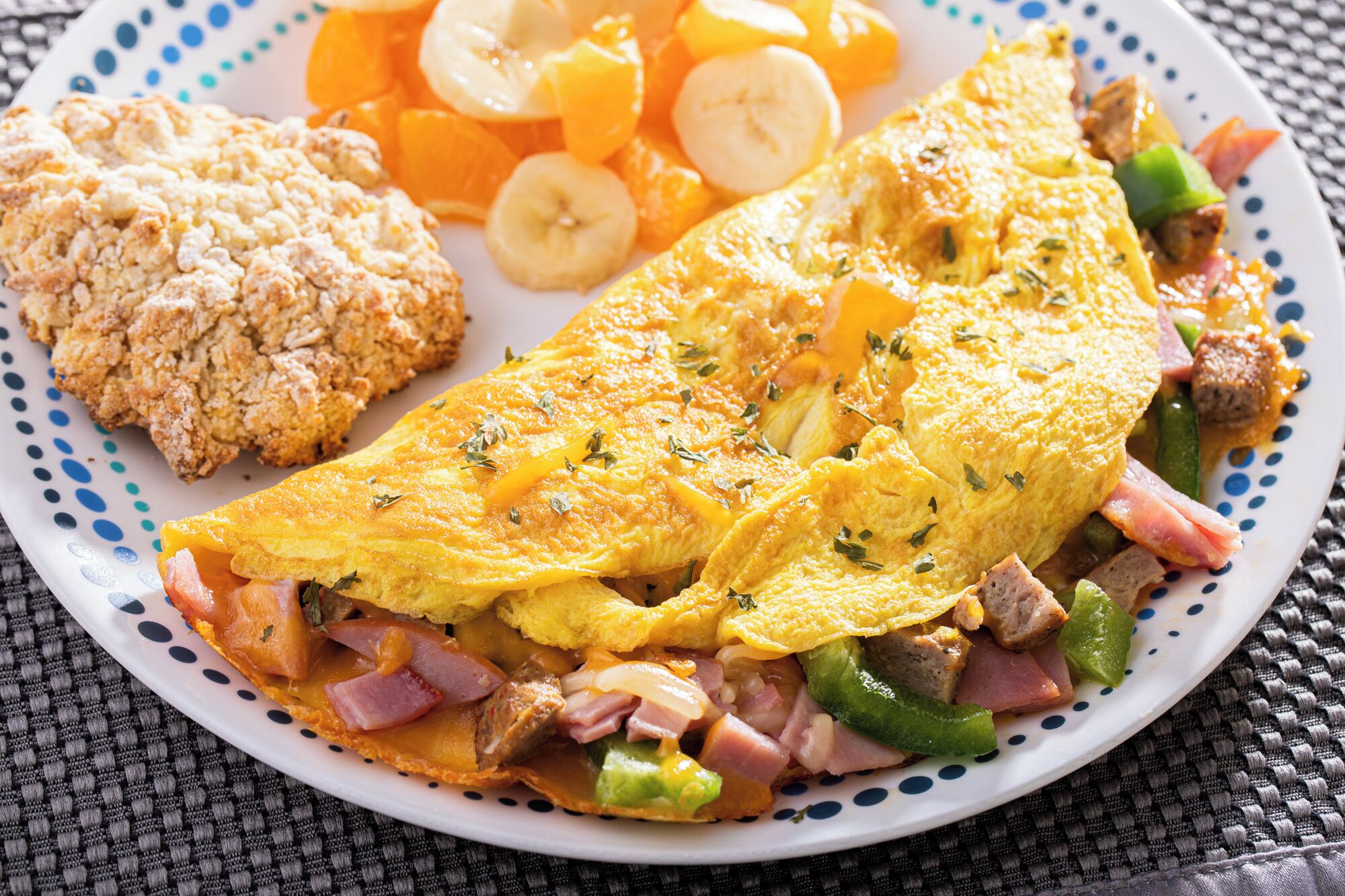 Une assiette contenant une omelette, du jambon, des poivrons et un biscuit.