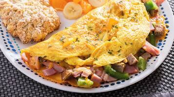 Une assiette contenant une omelette, du jambon, des poivrons et un biscuit.