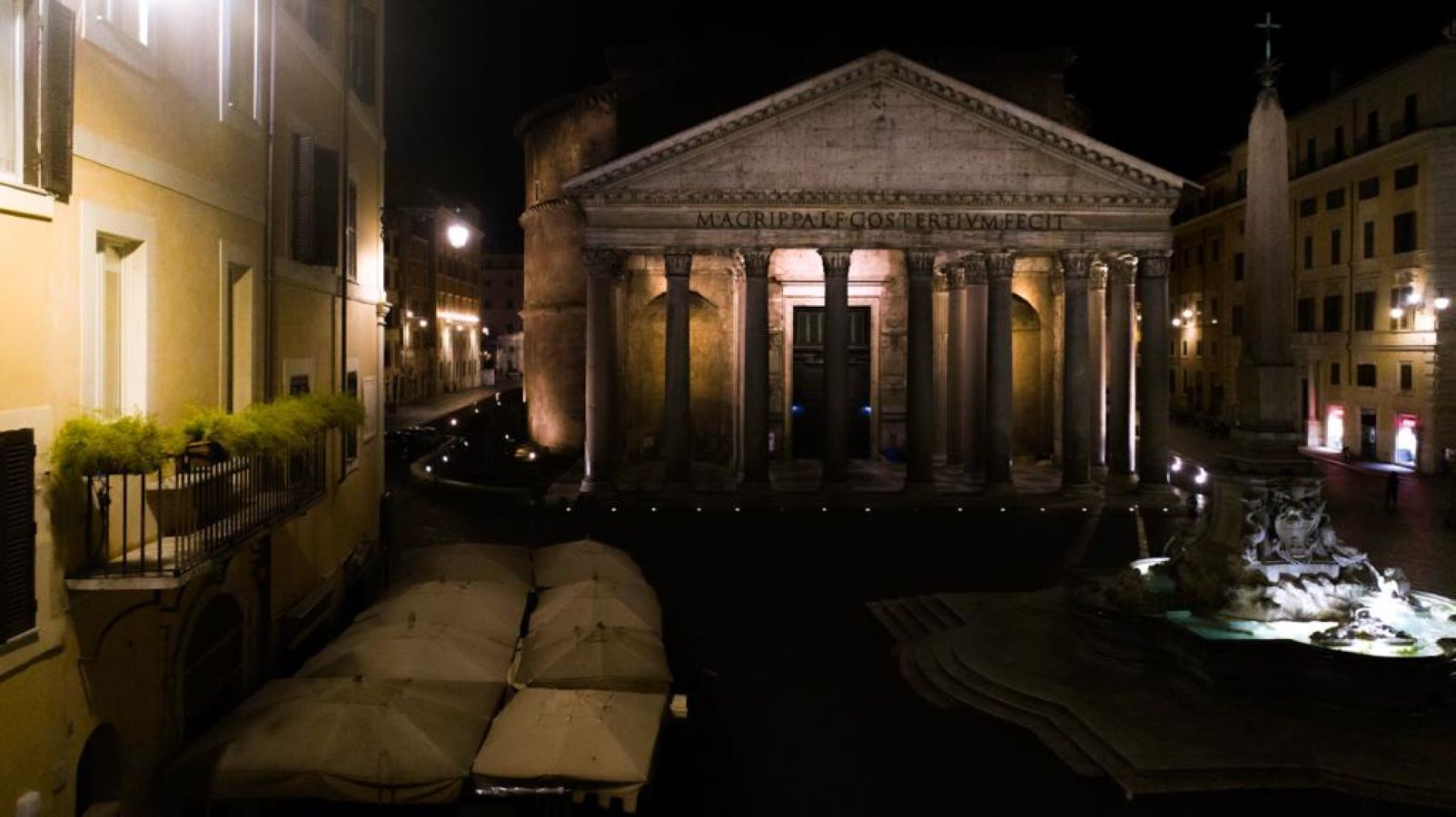 Ein klassizistisches Gebäude mit Säulen und einem zentralen Eingang, umgeben von einem Innenhof mit Brunnen und Sitzbereichen.