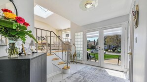 A modern interior with a staircase, a glass door leading outside, and a vase with flowers on a cabinet. - Prime Ryder Cup Location - Spacious 4 Bedroom Retreat with Pool, Outdoor Kitchen (Seaford)