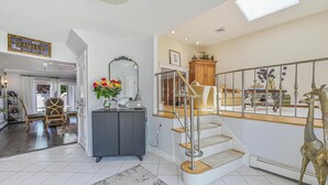 A spacious living area with a staircase, a family sign, a decorative mirror, and a giraffe statue. - Prime Ryder Cup Location - Spacious 4 Bedroom Retreat with Pool, Outdoor Kitchen (Seaford)