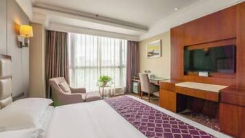 A hotel room with a bed, a desk, a chair, a TV, and a window with curtains.