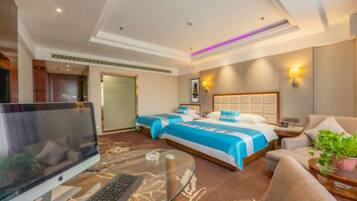 A hotel room with two beds, a desk with a computer, a TV, and a sofa.