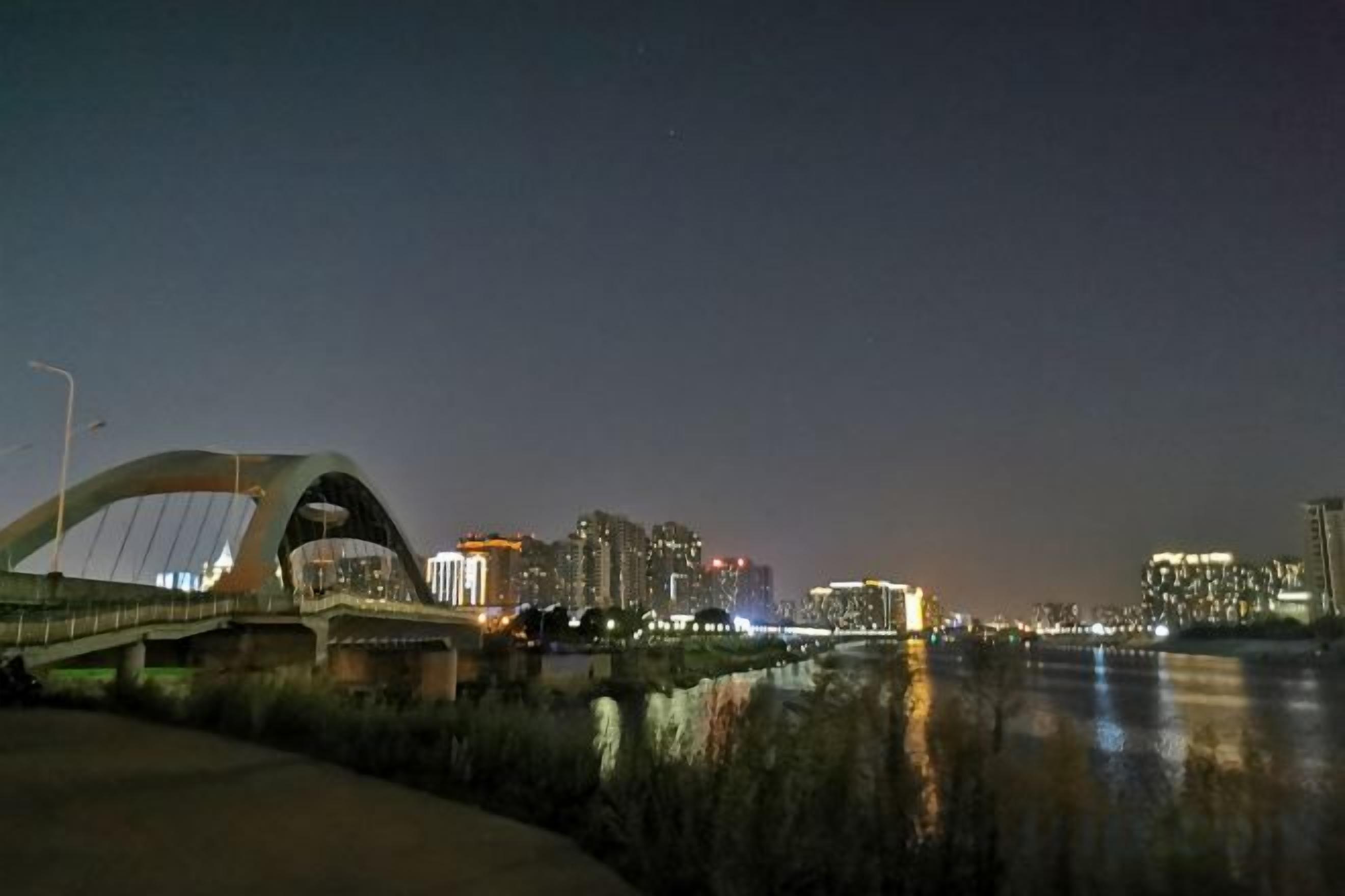 A nighttime cityscape with a bridge, buildings, and a river reflecting lights.