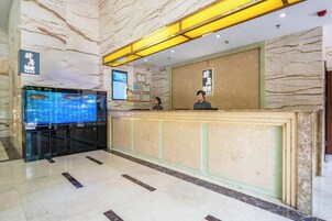 Zona de recepción de un hotel con mostrador de mármol, pantalla digital y recepcionista.