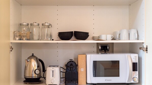 A kitchen with a kettle, toaster, microwave, and storage jars on the shelves.