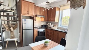 Cocina compacta con armarios de madera, un refrigerador de acero inoxidable, una estufa a gas y un comedor con mesa y sillas.