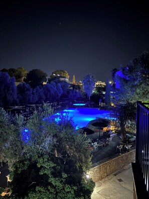Vue nocturne d’un espace piscine éclairé de lumières bleues, entouré d’arbres et d’immeubles.