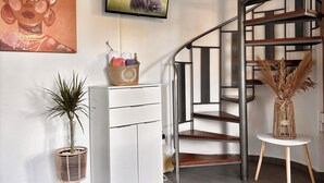 Un interior moderno con una escalera de caracol, un televisor de pantalla plana, un cuadro decorativo, una planta en maceta y una alfombra tejida.