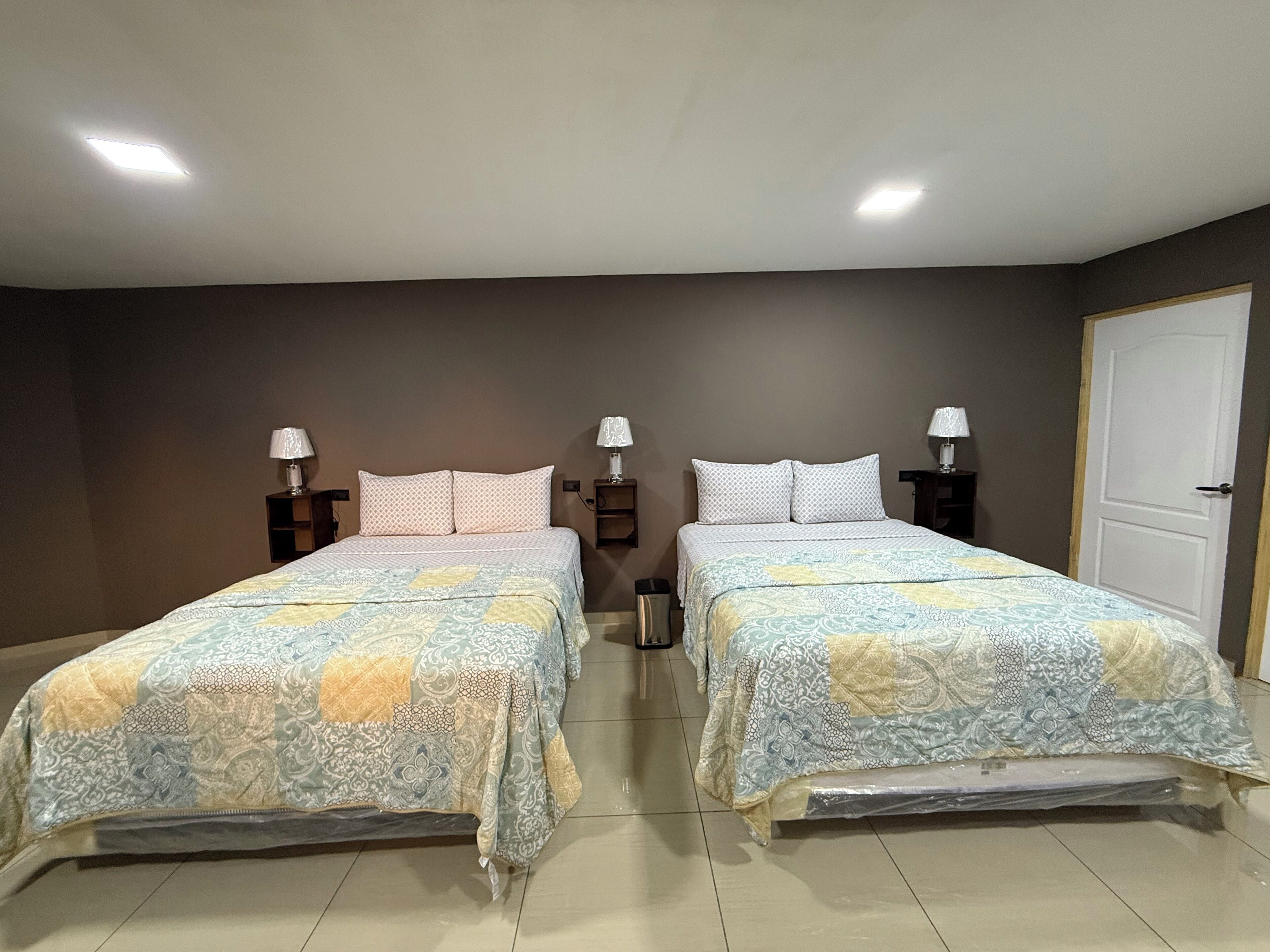 Une chambre d’hôtel avec deux lits, chacun recouvert d’une couvre-lit à motifs, dotée de lampes de chevet et dont la porte se trouve sur le côté droit.