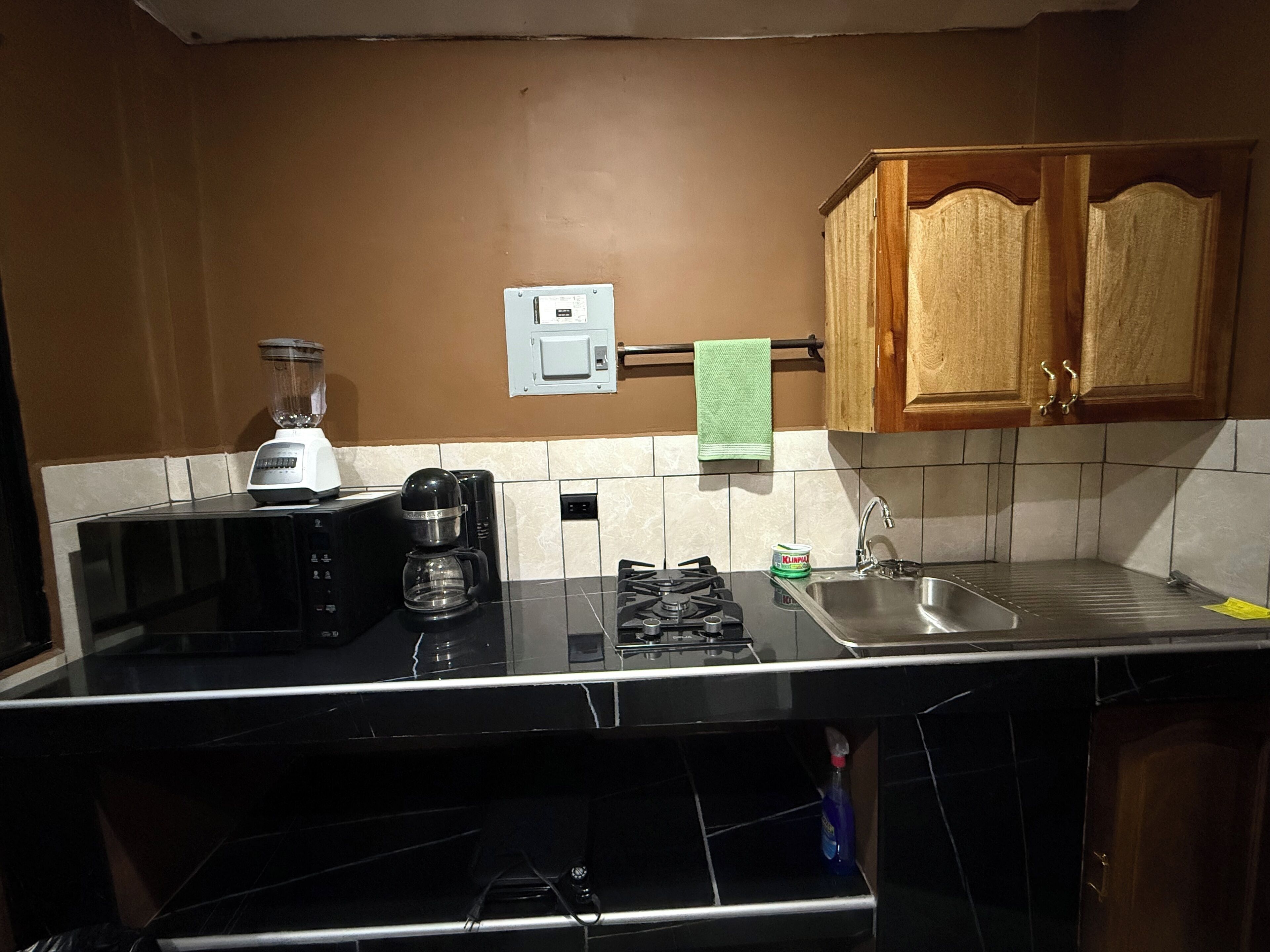 A kitchen with a black countertop, a blender, a coffee maker, a microwave, and wooden cabinets.