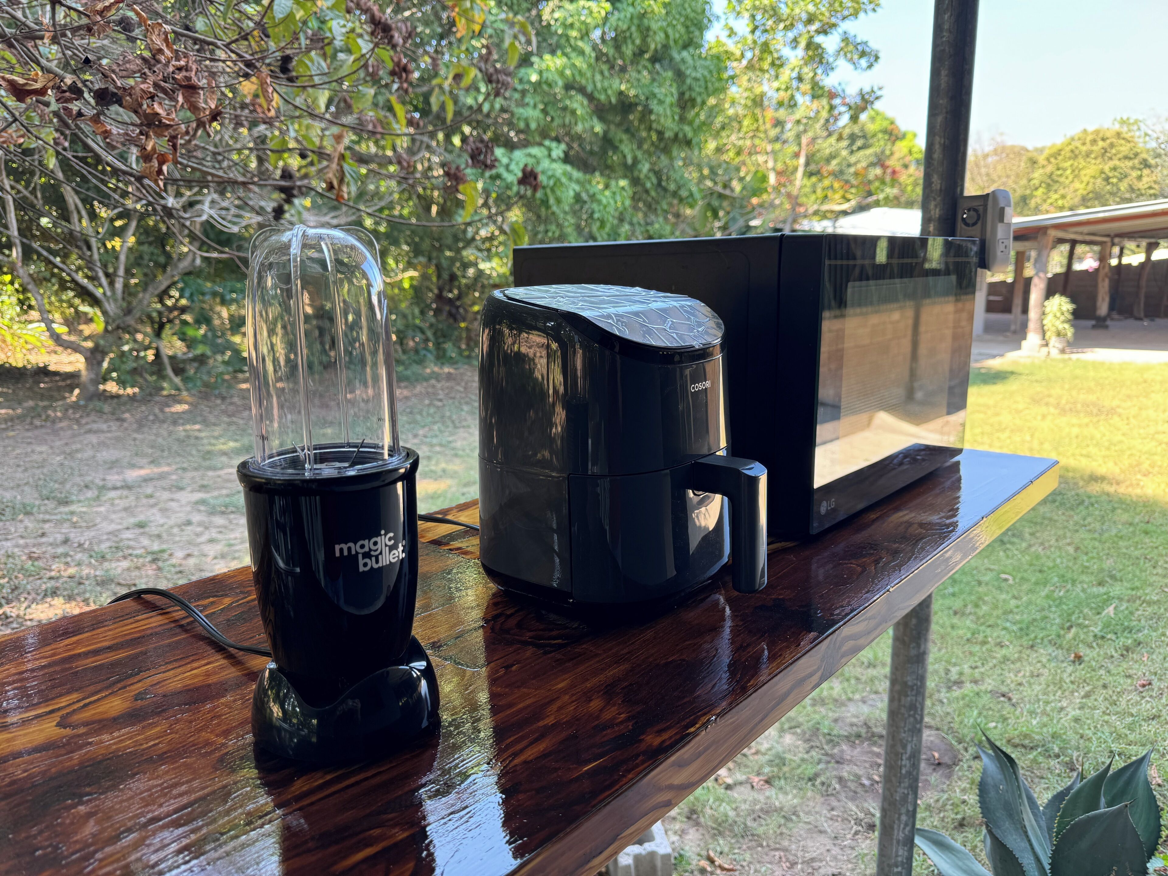 Una cafetera y una licuadora sobre una mesa de madera al aire libre.
