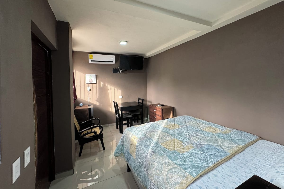 A bedroom with a bed, a desk, a chair, and an air conditioner.