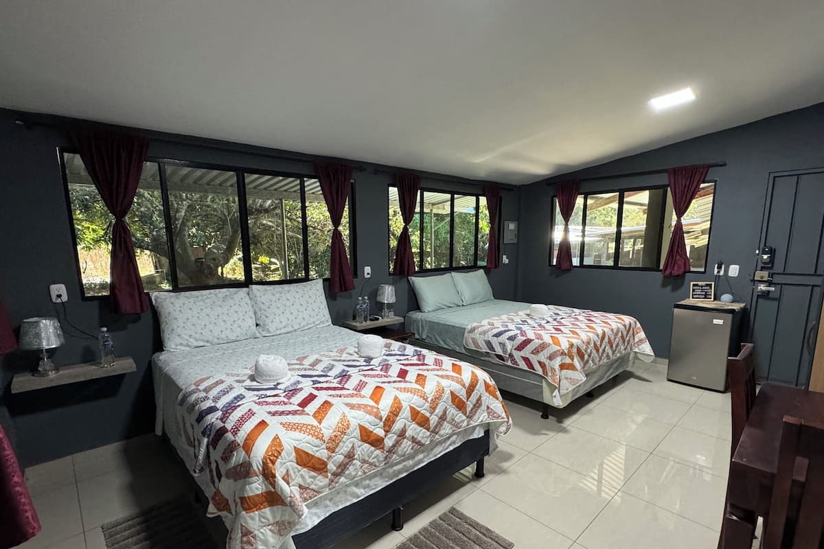 A hotel room with two beds, a small refrigerator, a desk, and a window with curtains.