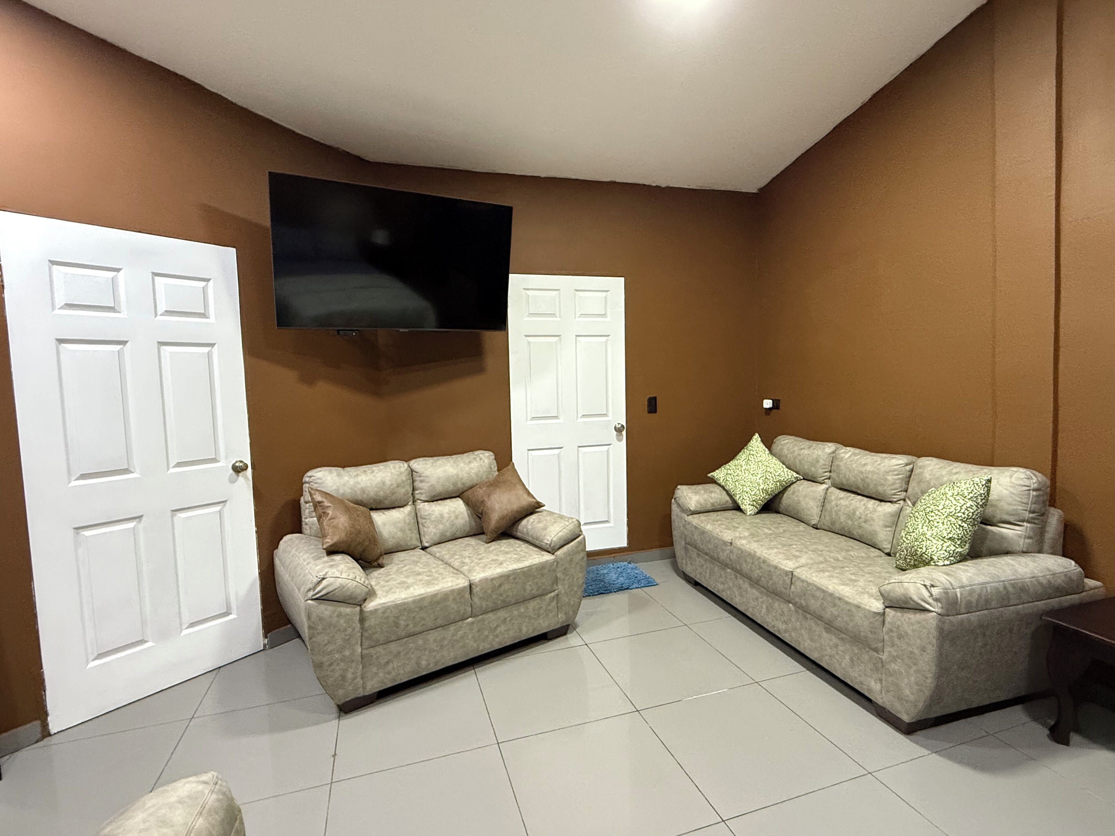 Una sala de estar con dos sofás, un televisor de pantalla plana montado en la pared y una puerta.