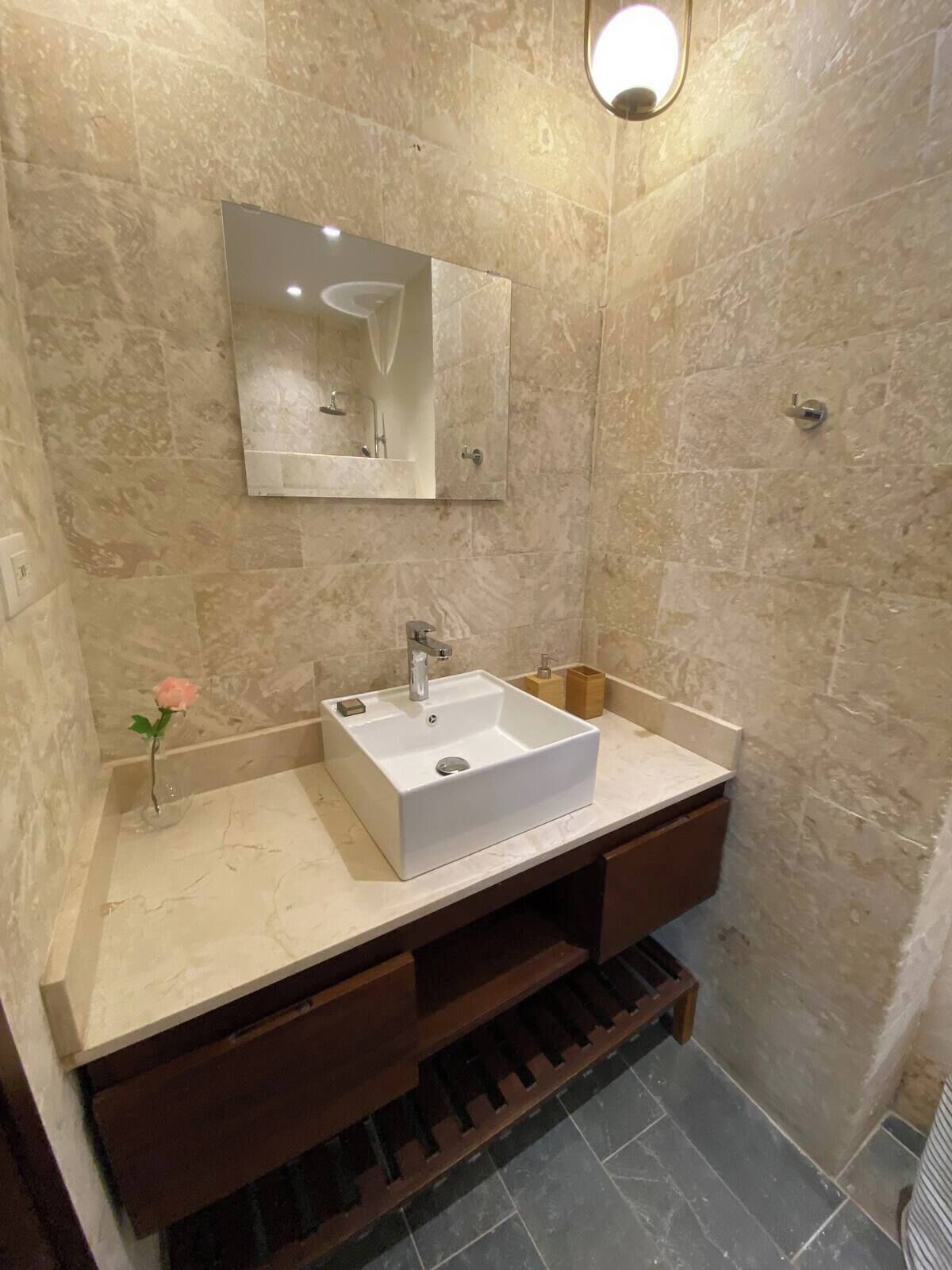 A modern bathroom with a white sink, a mirror, and a wooden vanity.