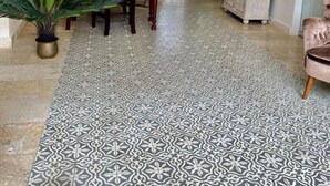 Un hall d’entrée spacieux avec un sol à motifs, un coin repas avec une table et des chaises en bois, une plante en pot et un grand miroir au mur.