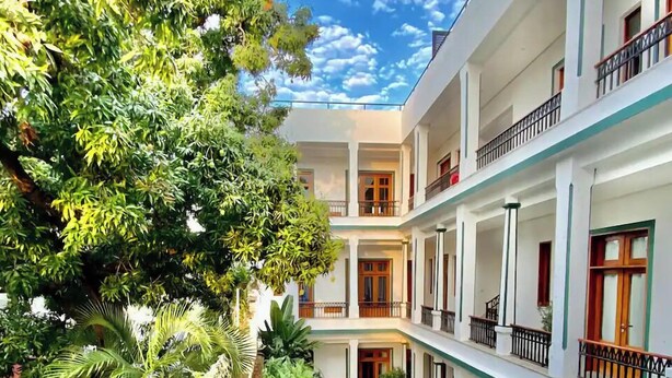 Un hôtel à plusieurs étages doté d’une cour intérieure où se trouve une piscine, le tout entouré d’une végétation luxuriante et d’arbres.