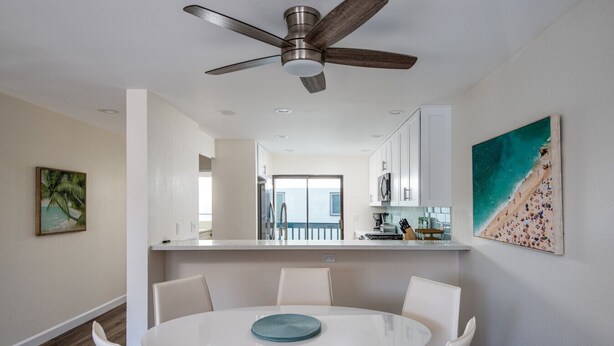 A modern kitchen with white cabinets, a dining area with a round table and white chairs, and a ceiling fan.