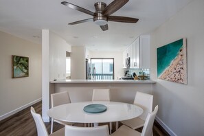 Una cocina moderna con armarios blancos, un comedor con una mesa redonda y sillas blancas, y un ventilador de techo.