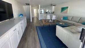 A modern living room with a white sofa, a blue rug, and a TV on a white cabinet.