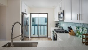 A modern kitchen with white cabinets, a stainless steel refrigerator, a gas stove, and a microwave.