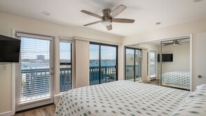 A bedroom with a large bed, a ceiling fan, and a balcony with a view of the water.