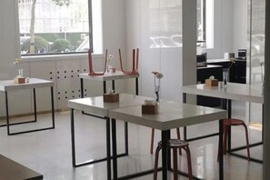 Een modern interieur met witte tafels en stoelen, een vaas met bloemen en een raam met uitzicht op gebouwen.