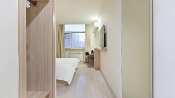 A hotel room with a bed, a desk, a chair, a radiator, and a window.