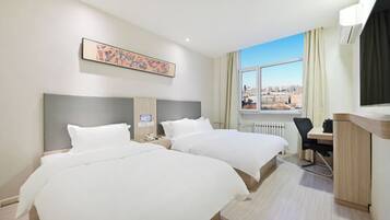A hotel room with two beds, a desk, a chair, a window with a city view, and a painting on the wall.