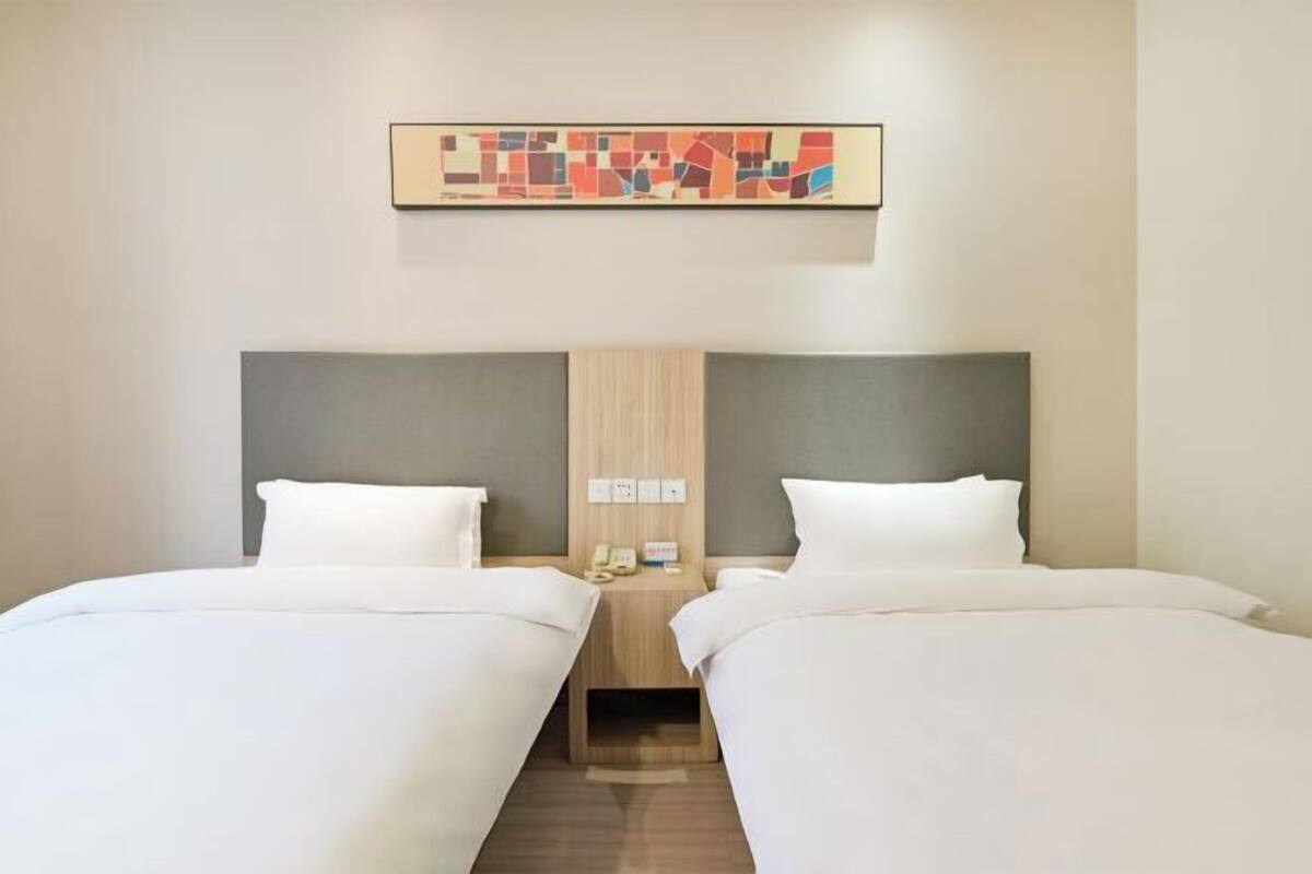 Una habitación de hotel con dos camas individuales, un cabecero de madera, una mesita de noche pequeña con un teléfono y una obra de arte colgada en la pared.