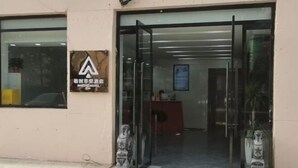Entrada de hotel con puerta de vidrio, un mostrador de recepción en el interior y un letrero con la marca del hotel.