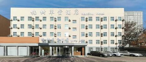 A hotel with a modern facade, multiple floors, and a parking area in front.