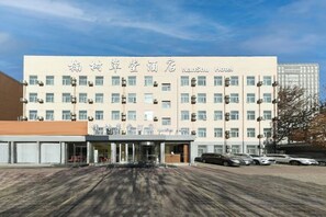 A hotel with a modern facade, multiple floors, and a parking area in front. - Nanshu Thatched Cottage Hotel (Huihua College Branch of Shijiazhuang Railway Station) (Shijiazhuang)